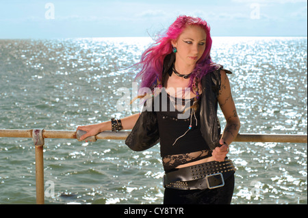 Les jeunes femmes/ fille aux cheveux rose et gilet noir et leggings debout devant la mer et le ciel Banque D'Images