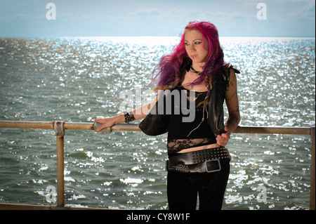 Les jeunes femmes/ fille aux cheveux rose et gilet noir et leggings debout devant la mer et le ciel Banque D'Images