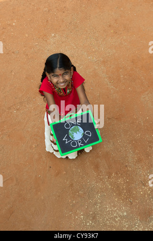 Village indien fille AVEC UN SEUL MONDE écrit sur un tableau noir dans un village de l'Inde rurale. L'Andhra Pradesh, Inde Banque D'Images