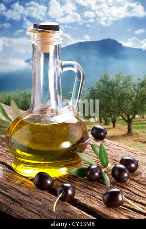 Olives noires avec une bouteille d'huile sur une table de bois sur un fond de jardin d'olive. Banque D'Images