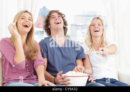 Trois friends eating popcorn en riant au salon Banque D'Images