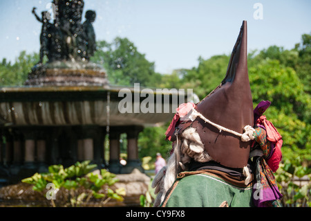 Un musicien ambulant en costume d'élève face à une fontaine de Central Park, à New York à l'été. Il ressemble à un gnome. Banque D'Images