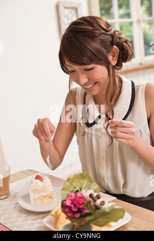 Jeune femme assise à table et manger un gâteau Banque D'Images