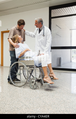 Médecin rire avec pregnant woman in wheelchair et partenaire Banque D'Images