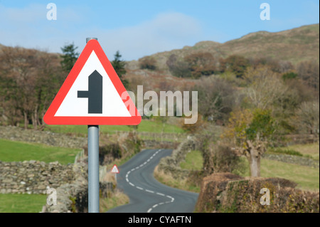 Un panneau routier qui indique une petite route à gauche situé à par une route de campagne sinueuse dans le Lake District, Cumbria, Royaume-Uni. Banque D'Images