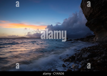 Le soleil se couche sur un ciel nuageux Cuillin ridge comme les vagues tour les rivages de Elgol Bay sur l'île de Skye. Banque D'Images