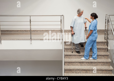 Aide infirmière femme âgée obtenir dans les escaliers Banque D'Images