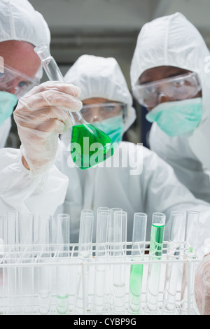 Chimistes dans les scaphandres de protection à la recherche de green liquid in beaker Banque D'Images