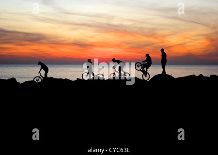 Les jeunes d'effectuer des Tours à vélos BMX, silhouetté par le coucher du soleil à West Bay, Dorset, UK Banque D'Images