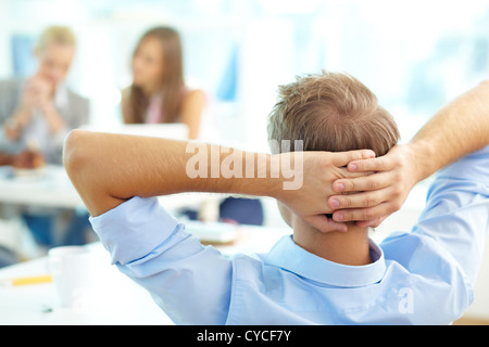 Vue arrière du professeur détendue laissant les mains derrière la tête et en regardant les étudiants travaillant Banque D'Images