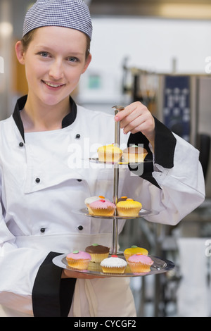 Smiling chef holding tiered cake tray Banque D'Images