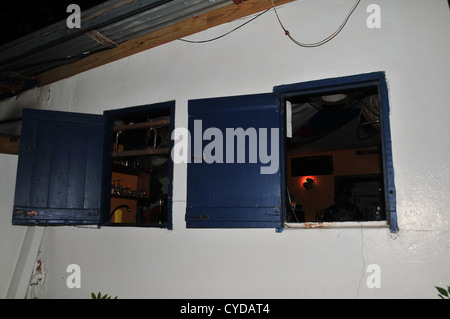 Vue de nuit en mur blanc, deux volets bleu ouvert les fenêtres, un coin cuisine, une tortue paresseuse Pizzeria, Tyrrel Bay, Carriacou, West Indies Banque D'Images