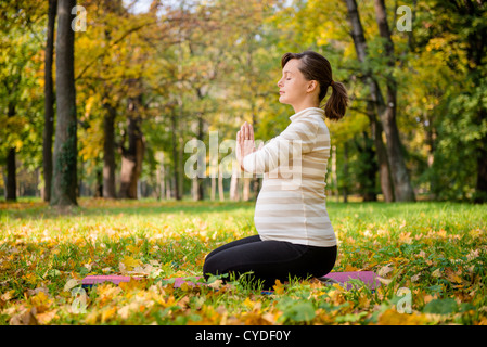 Jeune femme enceinte en méditant à l'extérieur dans le magnifique automne nature Banque D'Images
