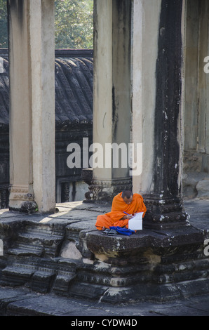 Un moine bouddhiste assis en face d'un temple à Angkor Wat, lecture. Banque D'Images