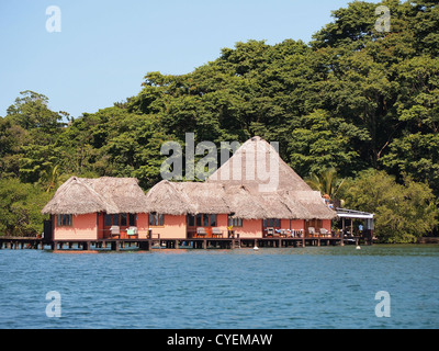 Tropical resort avec des bungalows au toit de chaume au-dessus de l'eau et des arbres en arrière-plan, l'Amérique centrale, le Panama Banque D'Images