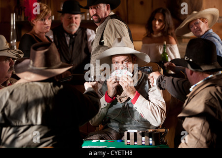 Un vieux cow-boy de l'ouest se cache derrières ses cartes après avoir été pris en train de tricher. Banque D'Images