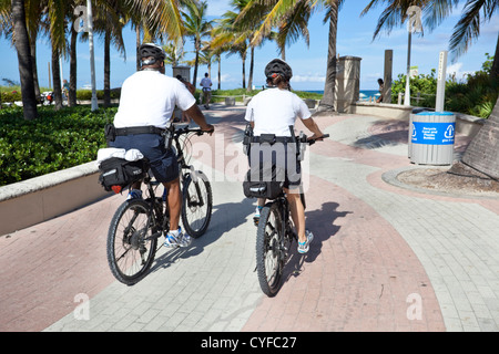 Vue arrière de deux policiers le patrouille à vélo le long de la promenade, Miami Beach, Floride, USA. Banque D'Images