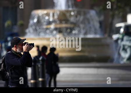 Un homme de prendre une photo à Trafalgar Square - une fontaine hors foyer dans l'arrière-plan Banque D'Images