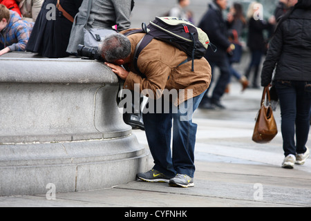 Un mâle affermissant sa caméra sur le mur d'une fontaine comme il prend une photographie à Trafalgar Square Banque D'Images