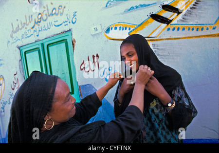 L'Égypte. Aswan. Les femmes de la tribu Nubienne en costume traditionnel en face de décorations sur mur. Banque D'Images