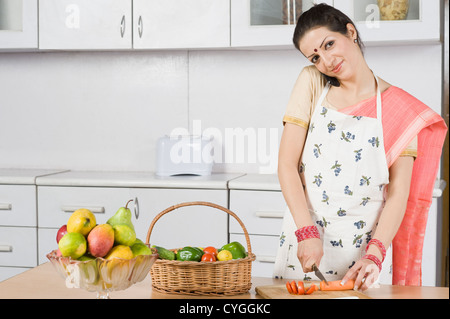 Woman cutting vegetables et parler dans un téléphone portable dans la cuisine Banque D'Images