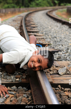 Garçon à l'écoute de l'approche des trains sur les lignes de chemin de fer au pont neuf à Demorada dans les hautes terres du Sri Lanka. Banque D'Images