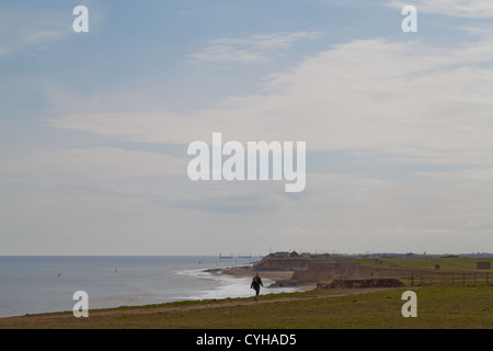 Lone walker sur falaise. Happisburgh beach et la côte. La défense de la mer brise-roche sur l'horizon. À au sud de parking collectif.Norfolk. L'East Anglia. Banque D'Images