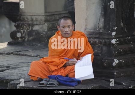 Un moine bouddhiste assis en face d'un temple à Angkor Wat, lecture. Banque D'Images