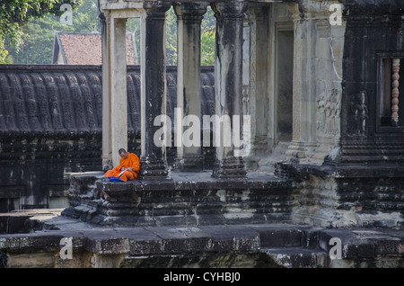 Un moine bouddhiste assis en face d'un temple à Angkor Wat, lecture. Banque D'Images
