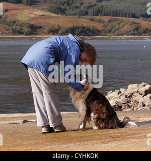 Femme en manteau bleu avec noir et blanc chien border collie par mer, Glenelg, Ecosse, Royaume-Uni Banque D'Images