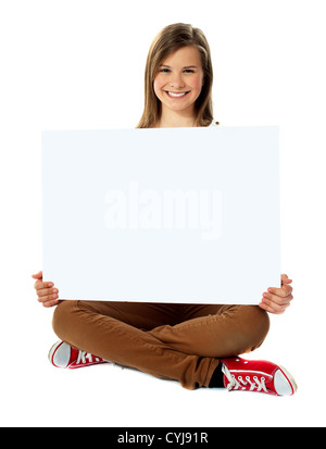 Joli sourire adolescent posant avec plaque en blanc, assis sur le plancher Banque D'Images