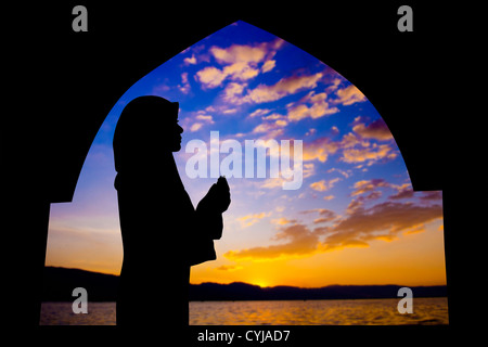 Silhouette de femme priant dans la mosquée musulmane pendant l'heure du coucher du soleil Banque D'Images