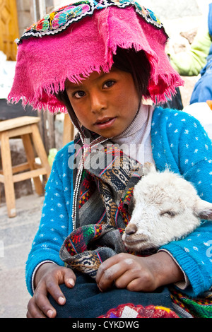 Pisac, Pérou, une jeune fille habillée de façon traditionnelle pose fièrement avec son agneau aussi sa famille vend leurs marchandises dans la Vallée Sacrée. Banque D'Images
