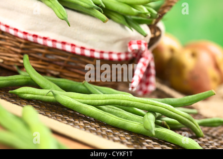 Haricots verts crus frais en face d'un panier avec des pommes de terre à l'arrière Banque D'Images