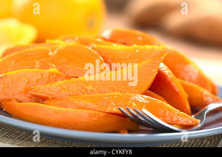 Quartiers de pommes de terre sucrée avec du sucre brun caramélisées et jus d'orange avec une fourchette sur une assiette, des oranges et des patates douces dans le Banque D'Images