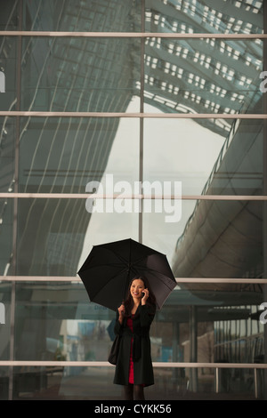 Asian businesswoman with umbrella on cell phone Banque D'Images