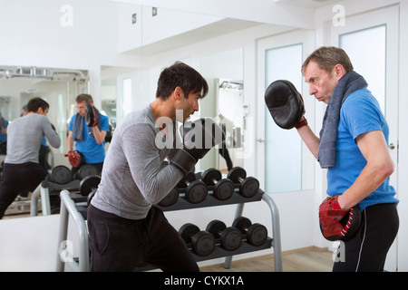 Boxer pratiquant avec formateur dans une salle de sport Banque D'Images