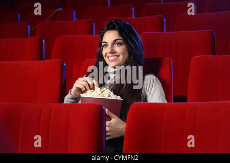 Film drôle : portrait d'une jolie fille dans un théâtre vide, elle mange du popcorn et sourires Banque D'Images