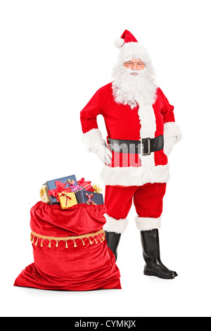 Portrait d'un Père Noël qui pose à côté d'un sac plein de cadeaux isolé sur fond blanc Banque D'Images