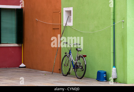 Un contraste de couleurs typiques de Venise, Burano, avec un vélo et des ustensiles de cuisine sur un mur vert citron avec orange derrière. Banque D'Images