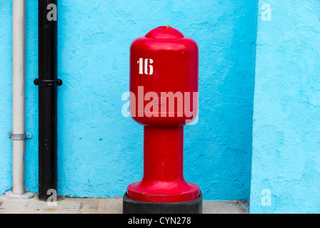 Un rouge lumineux de style vénitien d'incendie contre un mur bleu ciel avec tuyaux en noir et blanc en descendant. Banque D'Images