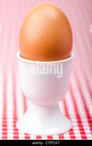 Un breakfastt œuf dans un coquetier sur red table vérifiées couvrir Banque D'Images