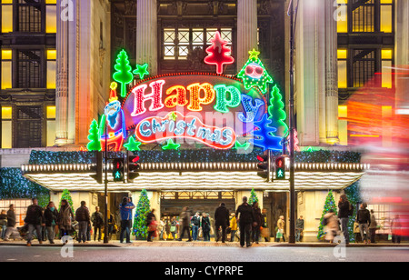London UK. Les acheteurs de Noël Xmas shopping à Selfridge's store Oxford Street avec de grandes lumières néons joyeux Joyeux Noël Banque D'Images