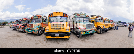 Bus de poulet Antigua Guatemala // ANTIGUA GUATEMALA, Guatemala — Panorama d'une variété de vieux bus scolaires américains peints de couleurs vives convertis en bus de poulet convergent dans le lot derrière le marché de la ville. Banque D'Images