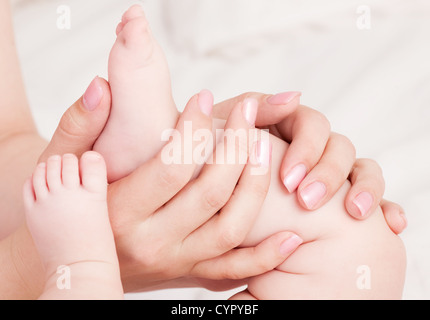 Mains de amother masser son bébé, pieds au lit à la maison Banque D'Images