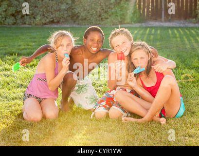 Des enfants assis dans l'herbe de manger les sucettes glacées Banque D'Images