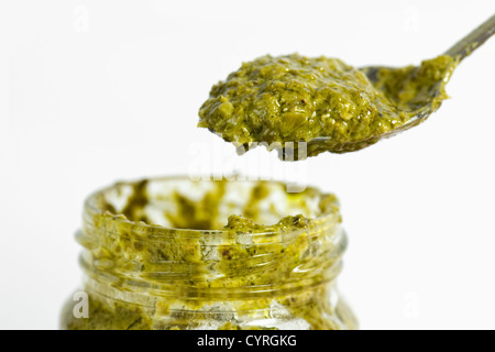 Close up of a3 cuillerée de pesto vert sur un fond blanc a tenu plus d'un pot ouvert Banque D'Images