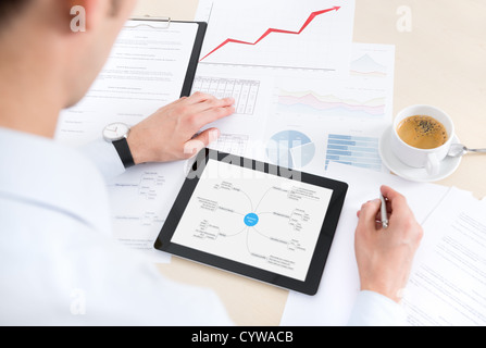 Businessman dans le milieu de travail avec des documents et à l'aide de tablette numérique moderne. Banque D'Images