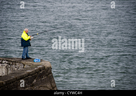 BEAUMARIS, pays de Galles — Un pêcheur solitaire jette sa ligne d'un vieux mur de pierre le long du front de mer de Beaumaris sur l'île d'Anglesey. La scène paisible capture l'attrait intemporel de la pêche à la ligne en mer avec pour toile de fond le détroit de Menai, avec les montagnes de Snowdonia visibles au loin. Cette image résume le charme tranquille et la beauté naturelle qui attirent les pêcheurs et les touristes dans cette pittoresque ville côtière galloise. Banque D'Images