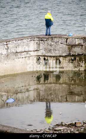 BEAUMARIS, pays de Galles — Un pêcheur solitaire jette sa ligne d'un vieux mur de pierre le long du front de mer de Beaumaris sur l'île d'Anglesey. La scène paisible capture l'attrait intemporel de la pêche à la ligne en mer avec pour toile de fond le détroit de Menai, avec les montagnes de Snowdonia visibles au loin. Cette image résume le charme tranquille et la beauté naturelle qui attirent les pêcheurs et les touristes dans cette pittoresque ville côtière galloise. Banque D'Images